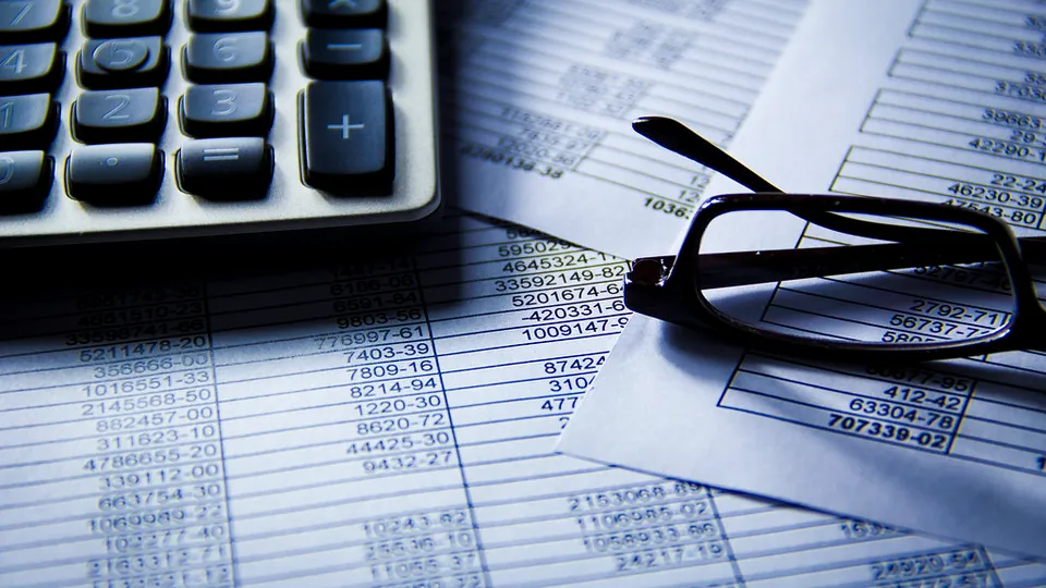 Calculator and reading glasses on printed financial spreadsheets