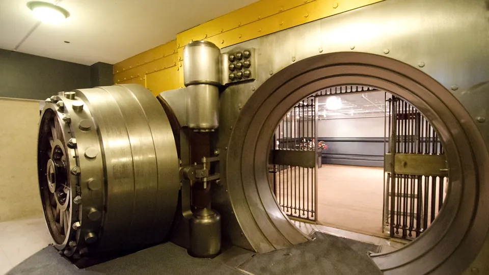 Open round steel bank vault door with a barred gate