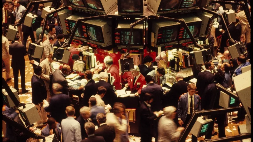 Crowded stock exchange trading floor with traders gathered around banks of monitors