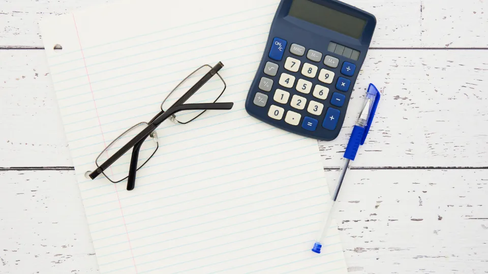 Blue calculator, reading glasses and a pen on a lined notepad